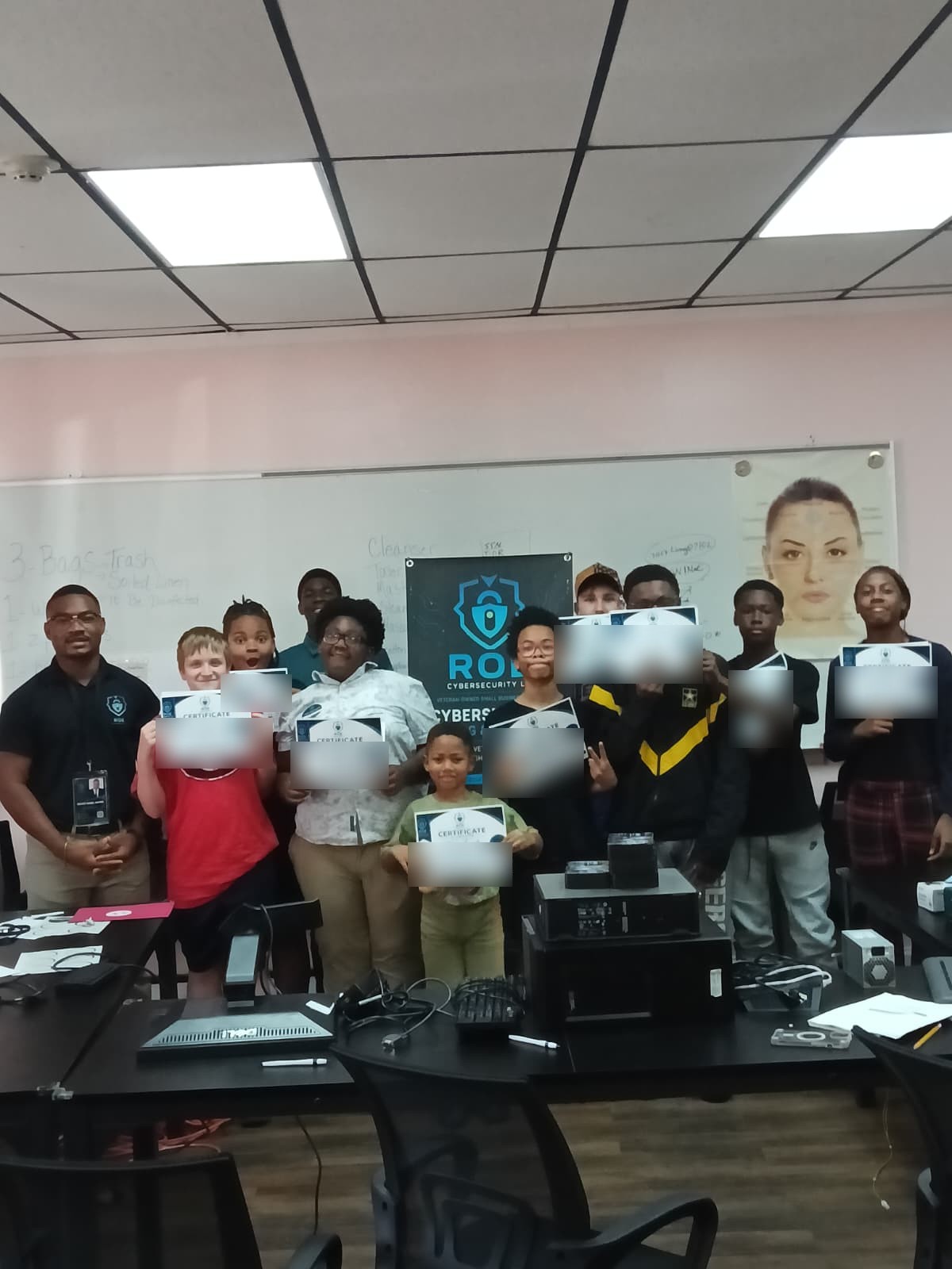 A large group of students holds ROE Cybersecurity certificates with an instructor in a classroom